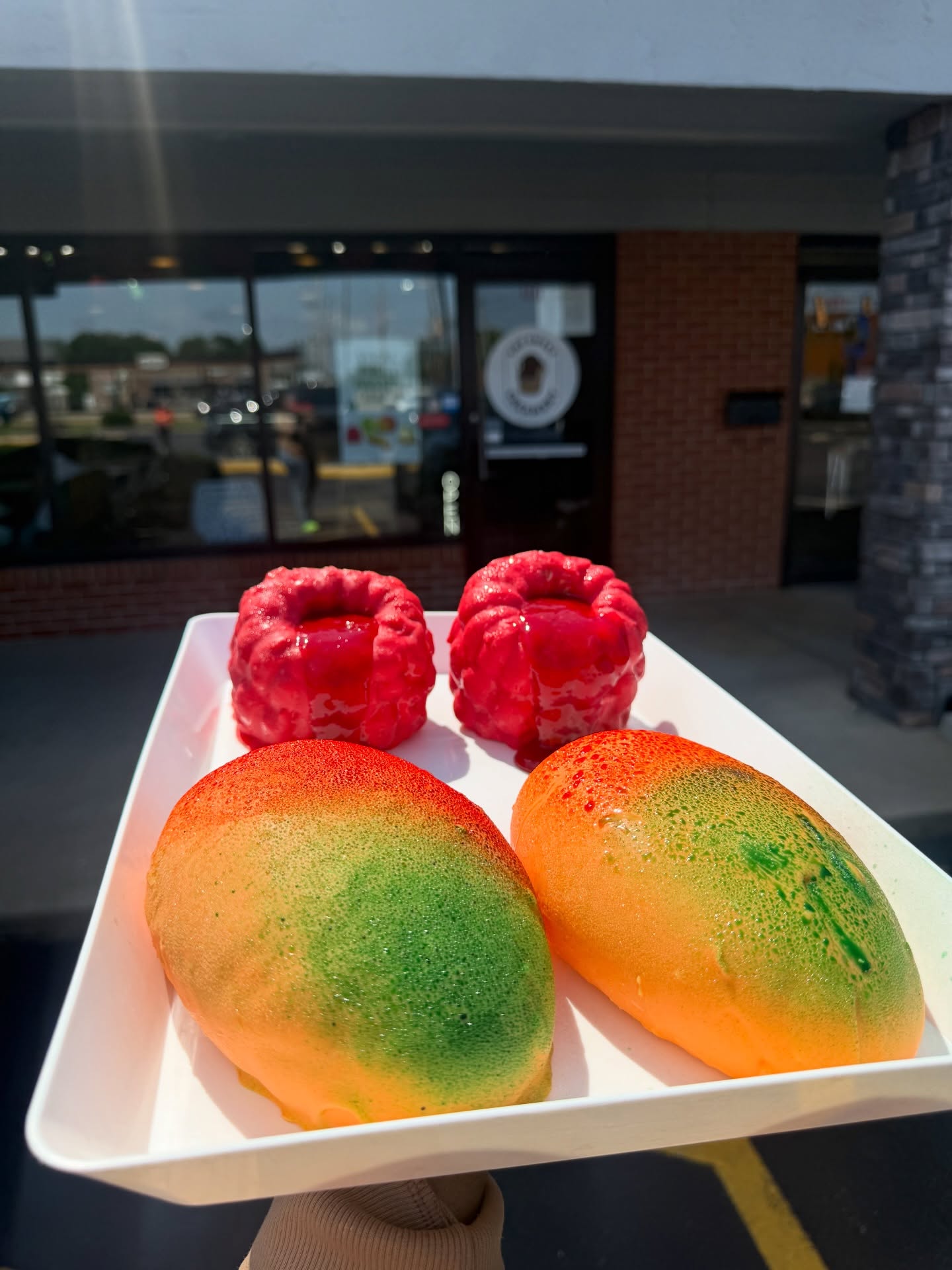 Fruit-shaped mousse pastries - Mega Mango and Mega Raspberry held outside the storefront