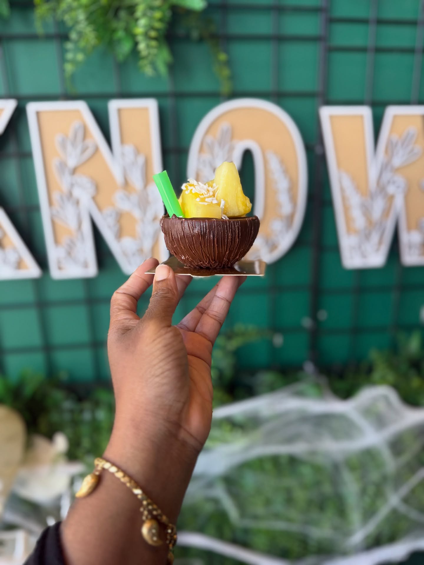 Chocolate shell pina colada cup held in front of the green interior wall